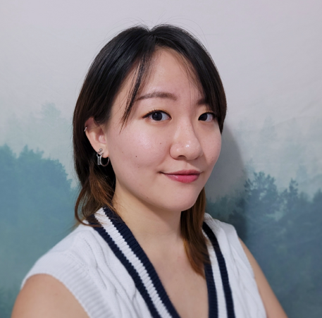 A headshot of a person with light skin, dark eyes, and brown hair. They are wearing a white sleeveless shirt.